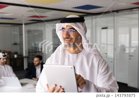 Smiling Middle Eastern businessman holding tablet in corporate office Smiling Middle Eastern businessman holding tablet in corporate office 143793875
