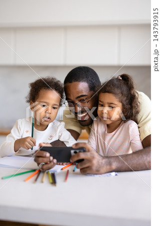 Black father and little biracial daughters watching cartoons on smartphone Black father and little biracial daughters watching cartoons on smartphone 143793915