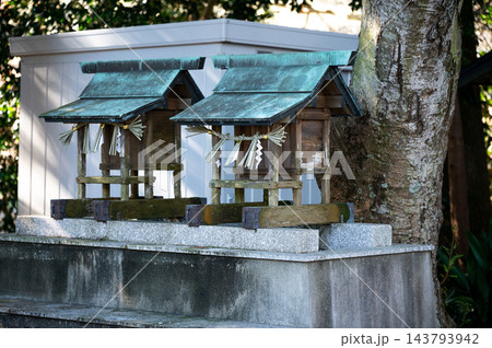 神社の境内に並んで祀られた二基の木造の小さな祠と注連縄、青緑色の屋根や石の台座を写した日本の信仰風景 神社の境内に並んで祀られた二基の木造の小さな祠と注連縄、青緑色の屋根や石の台座を写した日本の信仰風景 143793942