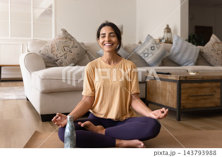 Happy young woman meditating on mat keeping water bottle near Happy young woman meditating on mat keeping water bottle near 143793988