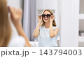 Caucasian woman trying on sunglasses standing in optician store 143794003