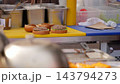 Delicious gourmet burgers stay positioned on yellow work surface during food stall assembly process. Tasty beef cutlets and fresh greens fill open buns beside metal kitchen supplies. 143794273