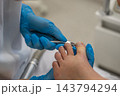 Clinician trims patients big toenail with stainless steel nippers in treatment room. Podiatry care focuses on precise nail grooming, with foot supported by gloved hands during careful trimming. 143794294