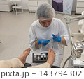 Careful specialist delivers pedicure treatment to person resting feet in chair, inspecting toenail condition while working with fine medical tools during clinical hygiene appointment. 143794302