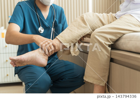 Healthcare professional examining senior patient's ankle at clinic for injury assessment. Healthcare professional examining senior patient's ankle at clinic for injury assessment. 143794336