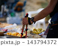 Hiker holding trekking poles at outdoor aid station with snacks and wristwatch 143794372
