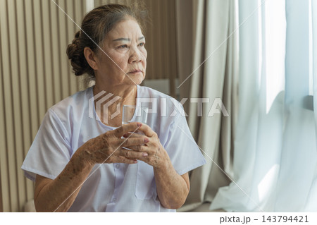 Senior woman reflecting while holding a glass of water at home for wellness. Senior woman reflecting while holding a glass of water at home for wellness. 143794421