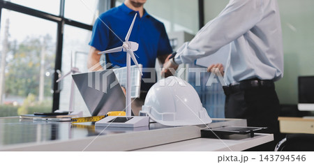 Two Asian engineers wearing hardhats and safety vests discussing solar panel installation and renewable energy project in the office. 143794546