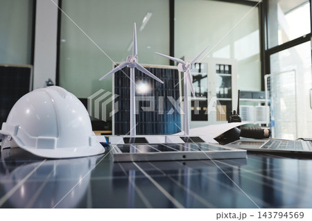 Two Asian engineers wearing hardhats and safety vests discussing solar panel installation and renewable energy project in the office. 143794569
