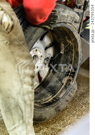 Mechanic repairs vehicle tire during pit stop at racing event in the afternoon on a warm day Mechanic repairs vehicle tire during pit stop at racing event in the afternoon on a warm day 143795354
