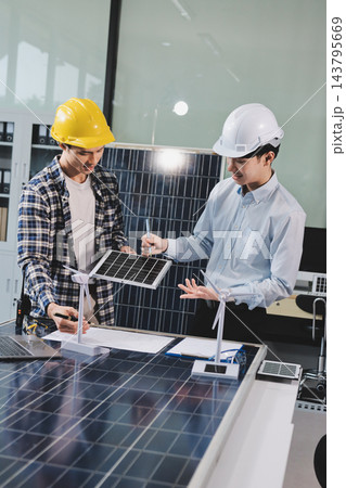 Two Asian engineers wearing hardhats and safety vests discussing solar panel installation and renewable energy project in the office. Two Asian engineers wearing hardhats and safety vests discussing solar panel installation and renewable energy project in the office. 143795669