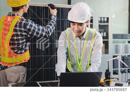 Two Asian engineers wearing hardhats and safety vests discussing solar panel installation and renewable energy project in the office. Two Asian engineers wearing hardhats and safety vests discussing solar panel installation and renewable energy project in the office. 143795687