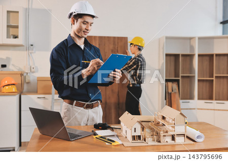 Asian architect and engineer team checking architectural house model using measuring tape on the table at office studio. 143795696