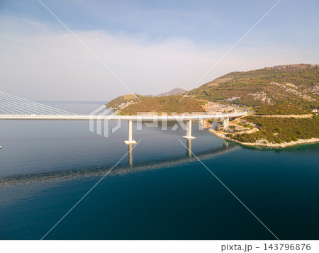 Modern cable stayed bridge curves along rocky coast above clear water, supported by concrete piers and fine cables. This major crossing highlights practical bridge engineering in scenic setting. 143796876