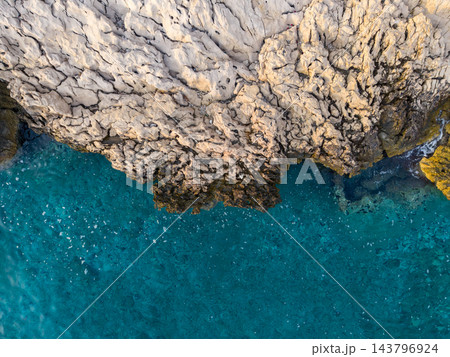 Makarska, Croatia coastline displays pale jagged limestone above vivid blue green sea. Rocky coastal ledges and transparent Adriatic water form striking natural pattern from overhead. 143796924
