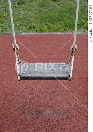 An empty wooden swing at a playground with a red rubber surface An empty wooden swing at a playground with a red rubber surface 143797168