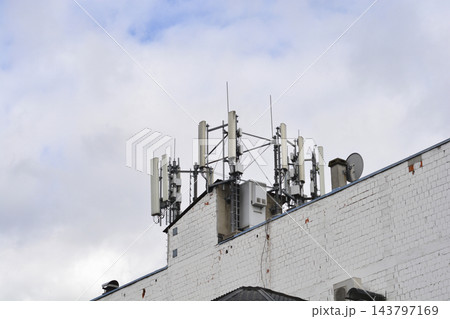 A cellular network base station on a building roof against a cloudy sky 143797169