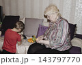 An elderly woman a grandmother brings fruit on a plate to her young grandson in the room and feeds him. Caring for children and the elderly parental love. 143797770