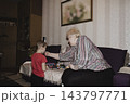 An elderly woman a grandmother brings fruit on a plate to her young grandson in the room and feeds him. Caring for children and the elderly parental love. 143797771