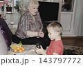 An elderly woman a grandmother brings fruit on a plate to her young grandson in the room and feeds him. Caring for children and the elderly parental love. 143797772