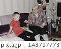 An elderly woman a grandmother brings fruit on a plate to her young grandson in the room and feeds him. Caring for children and the elderly parental love. 143797773