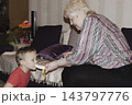 An elderly woman a grandmother brings fruit on a plate to her young grandson in the room and feeds him. Caring for children and the elderly parental love. 143797776