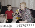 An elderly woman a grandmother brings fruit on a plate to her young grandson in the room and feeds him. Caring for children and the elderly parental love. 143797777