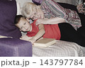 grandmother is reading colorful book grandson, has leaned in closer to listen. grandmother wearing glasses, boy, dressed red T-shirt, is intently examining the book and listening to the story. 143797784