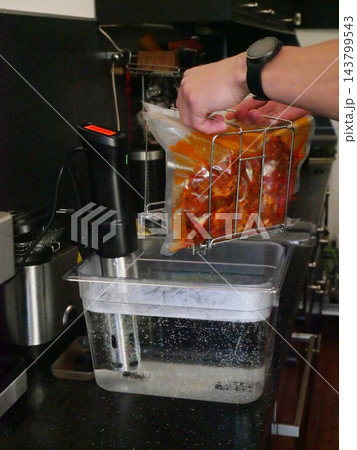 Cook placing vacuum sealed meat bag into sous vide water bath machine. Sous-vide culinary technique for precise temperature food preparation. Professional kitchen appliance for cooking. Cook placing vacuum sealed meat bag into sous vide water bath machine. Sous-vide culinary technique for precise temperature food preparation. Professional kitchen appliance for cooking. 143799543