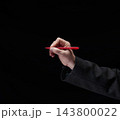 Man's hand in a suit jacket holding a red pen ready to write or sign a document on a dark background 143800022