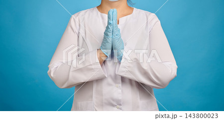 Doctor in a white coat and blue medical gloves holding hands in a praying or pleading gesture, medic hoping for recovery 143800023
