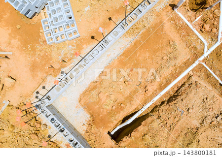 Workers are pouring concrete for foundation while machinery moves earth at building site in city. 143800181