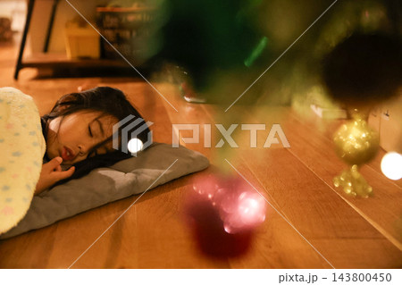 クリスマスツリーのそばで毛布をかけて眠る子ども クリスマスツリーのそばで毛布をかけて眠る子ども 143800450