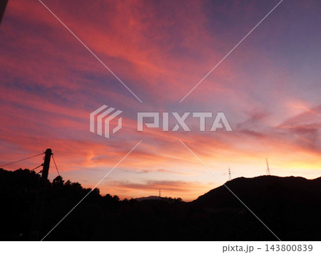 鮮やかな茜色と紫が織りなすドラマチックな夕焼け空と山並みのシルエット 143800839