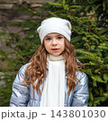 Young girl in white beanie and scarf portrait next to evergreen tree on a winter day 143801030