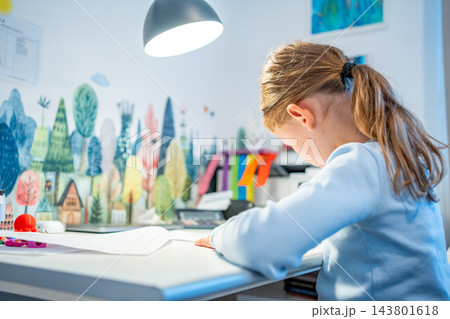 First grade girl practices handwriting at desk in her room. Child studies at home at beginning of school year with selective focus and soft background First grade girl practices handwriting at desk in her room. Child studies at home at beginning of school year with selective focus and soft background 143801618