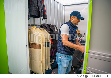 Man organizes personal belongings inside a rented self storage unit. Self storage provides extra space for furniture, clothes and household possessions Man organizes personal belongings inside a rented self storage unit. Self storage provides extra space for furniture, clothes and household possessions 143801621