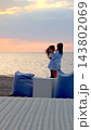 Two women share affectionate moment on beach at sunset, one holding smartphone near her companion. Their tender pose and calm seaside setting suggest romantic getaway by water, with both women close 143802069