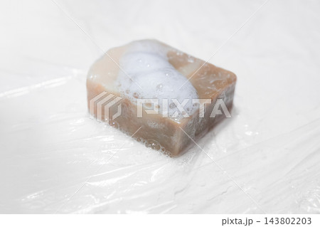 Brown soap bar with white foam on translucent surface. Bubbles from natural cleanser for hygiene and personal care. Brown soap bar with white foam on translucent surface. Bubbles from natural cleanser for hygiene and personal care. 143802203