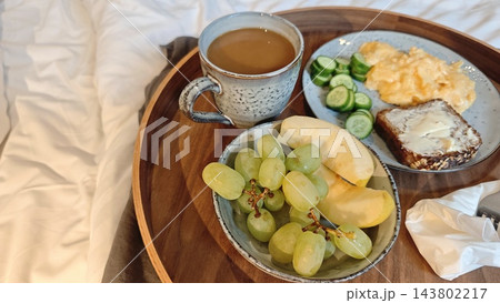 Breakfast tray with coffee, fruit, eggs, cucumber, toast, and butter arranged on a bed, inviting morning meal served in bed setting 143802217