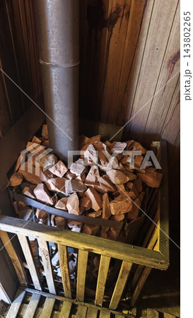 Metal stove pipe rising above a basket of irregular stones beside dark wooden wall panels in a rustic indoor setting 143802265