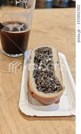 An open faced sandwich with a dark textured topping rests on a paper plate beside a partially filled glass of dark beer on wood An open faced sandwich with a dark textured topping rests on a paper plate beside a partially filled glass of dark beer on wood 143802302