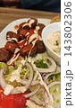 Meatballs with creamy sauce, salad, tomato, and dip arranged on a white plate over a wooden table, close up of a plated meal 143802306