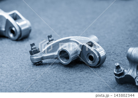 Close-up of automotive roller rocker arm parts in a modern blue tone scene 143802344