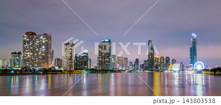 Bangkok riverfront skyline with illuminated skyscrapers and Ferris wheel at blue hour, modern high rise architecture reflecting on Chao Phraya River for urban travel and city life concept. Bangkok riverfront skyline with illuminated skyscrapers and Ferris wheel at blue hour, modern high rise architecture reflecting on Chao Phraya River for urban travel and city life concept. 143803538