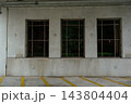 A concrete parking garage wall shows three dark windows and yellow parking lines. Reflections of trees appear in the glass under bright overhead lighting. 143804404