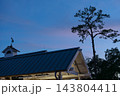 A Winter Park station roof sits below a tall tree silhouette in the blue evening sky. The quiet architectural detail includes warm station lights, treetops, and soft twilight color. 143804411