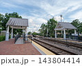 A Winter Park train station shows railroad tracks, platforms, and white covered shelters under a cloudy blue sky. The transportation scene includes brick paving, safety railings, trees, and an empty 143804414