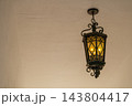 A vintage hanging lantern glows with warm light against a plain ceiling. The ornate metal frame and soft shadows create a classic architectural detail. 143804417