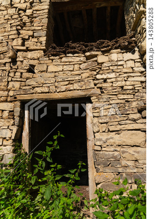 Stone building ruin with wooden doorway and foliage 143805288